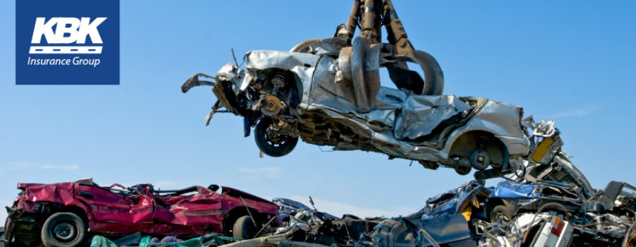 Crane holding demolished car in the air among field of wrecked cars